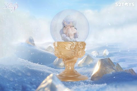 This 52Toys “Sleep: Life of Fantasies” figurine showcases a peaceful character curled up inside a sparkling snow globe, seated atop an ornate golden base. Surrounded by snowy terrain and shimmering crystal peaks, the soft pastel figure appears to be in deep slumber, evoking a sense of stillness and winter serenity.
