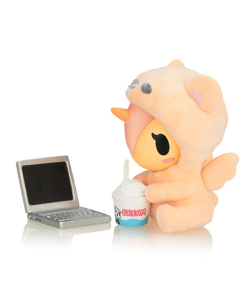 Cuddle Bear in a peach-toned bear onesie, sitting beside a miniature silver laptop and a small cup of "Cream" soft serve.