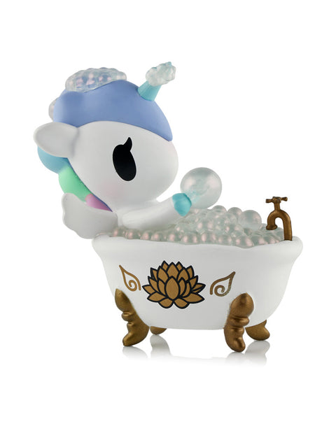 A white and blue Unicorno figure sitting inside a white clawfoot bathtub filled with iridescent bubbles and a gold lotus design on the side.