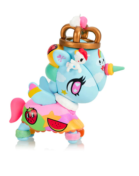 A sky-blue Unicorno wearing a large golden crown features a rainbow horn, cloud motifs, and a tiny white character perched on top. Its multicolored skirt shows fruit graphics such as strawberries and watermelon slices. Bright wings, pastel hooves, and vibrant star details create a bold, energetic, color-splashed appearance.