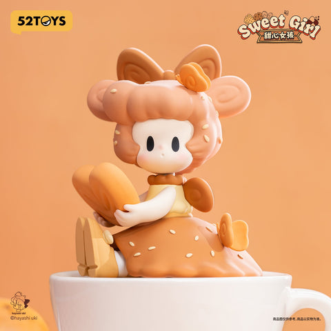 A secret edition figurine with chestnut brown hair styled in curls, wearing a checkered dress and giant bow. She hugs a butterfly-shaped cookie, eyes closed in blissful contentment.