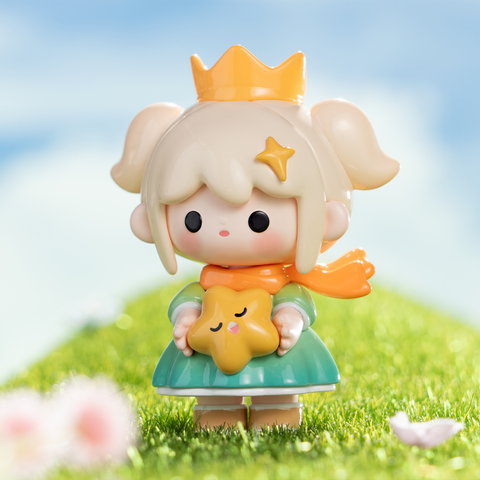 A blonde girl styled as the Little Prince wears a green outfit, golden crown, and orange scarf. She holds a smiling golden star plush with closed eyes. The bright meadow backdrop emphasizes a dreamy fairy-tale aesthetic, capturing themes of innocence, exploration, and storybook wonder.