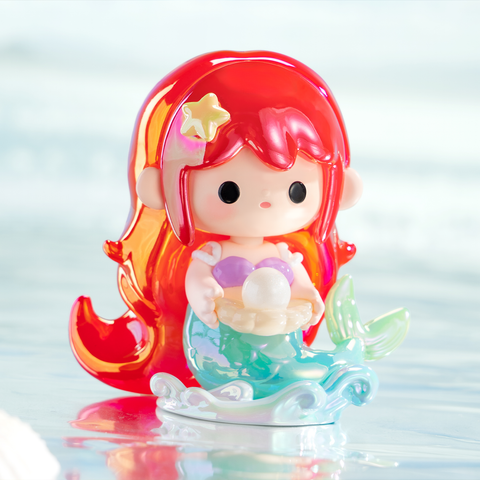 A vibrant mermaid figurine with flowing red hair and a golden star clip. She has a lavender seashell top and shimmering turquoise tail, holding a clam shell with a pearl inside. Translucent waves accent her design, capturing magical ocean fantasy and undersea wonder.