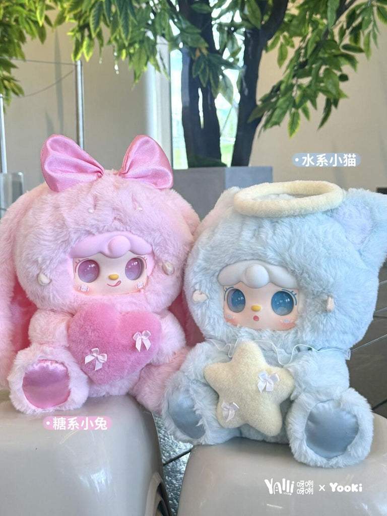 Two large plush characters sit side by side: a pink bunny with a satin bow and heart pillow, and a pale blue kitten with a fluffy halo and a soft star cushion. Both have pastel facial details with glassy eyes and rounded paws, evoking a dreamy idol aesthetic.