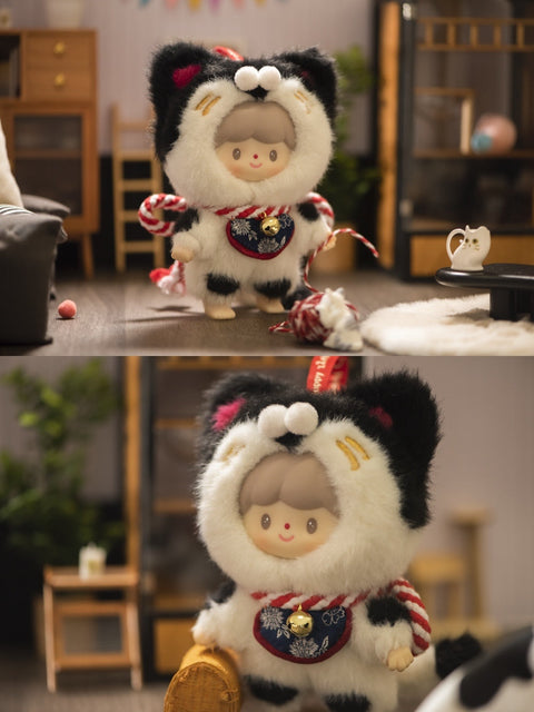 Two photos of a plush figure from the Finding Unicorn x 卓大王 “My Little Cat Series” blind box collection, featuring the secret hidden edition named Blessing Cat. The doll has a sweet face, gray hair, and wears a soft white and black cat costume with red and gold details, including a red rope, a floral bib with a gold bell, and tiny cat ears. The background is a cozy miniature room setup with furniture, cat toys, and home decor, giving a warm, playful atmosphere.